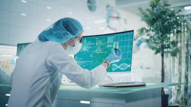 female scientist testing medical marijuana, making notes. team working in background. charts and models on computer screens. modern laboratory interior - medical marijuana imagens e fotografias de stock