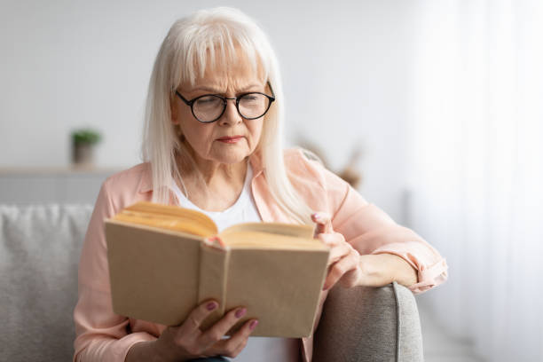 mujer madura enfocada en gafas tratando de leer libros - women poverty senior adult mature adult fotografías e imágenes de stock