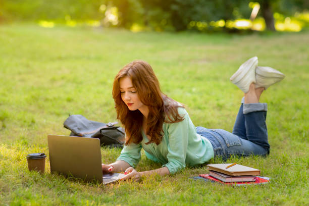 istock Beautiful redhead university student girl using laptop outdoors, studying remotely from park 1319039064