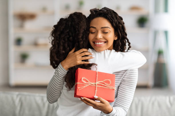 istock Cheerful black lady with gift box hugging her daughter 1319039148