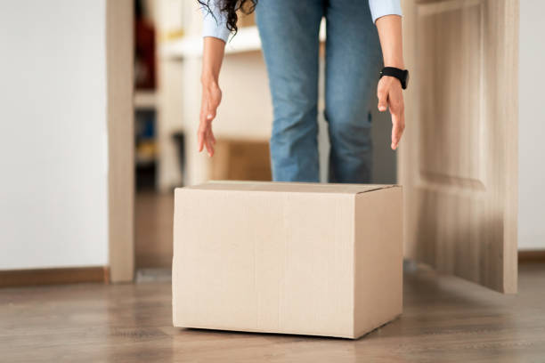 Unrecognizable woman picking cardboard box up from the floor