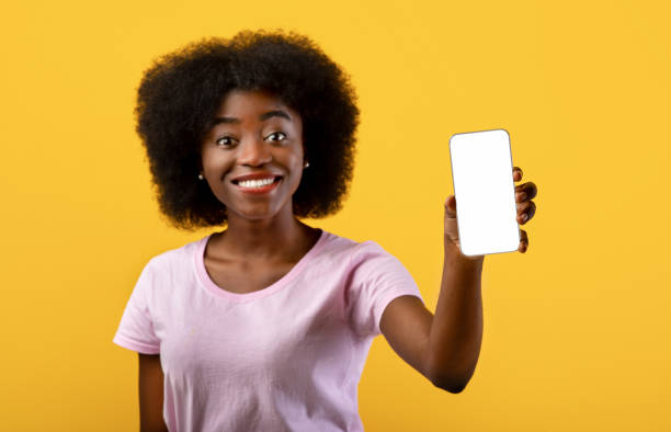 istock Great app concept. Cheerful black woman demonstrating smartphone with empty screen, standing against yellow background 1319041730