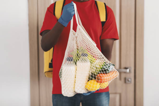 istock Black delivery man holding net mesh bag with groceries 1319041788