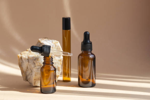 istock Empty brown glass bottles, with open and closed dropper lids, for cosmetics, oils, creams, standing next to marble stone. Soft shadows from objects fall on beige background 1319044358