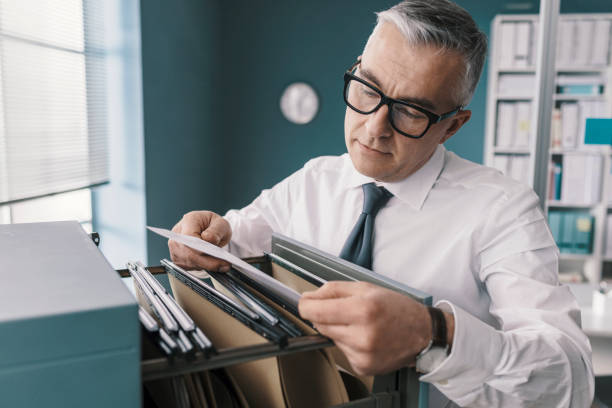 Businessman searching for files and documents Corporate businessman searching for paperwork in the filing cabinet filing cabinet photos stock pictures, royalty-free photos & images
