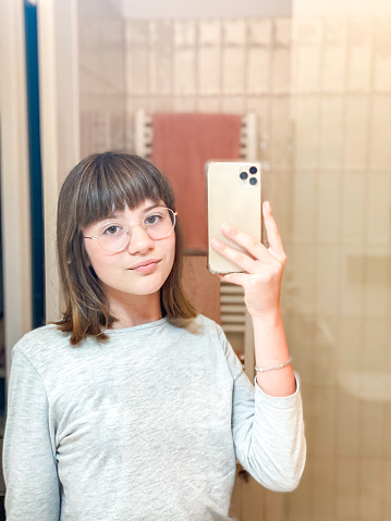 Girl taking a selfie in front of the bathroom mirror with a mobile phone