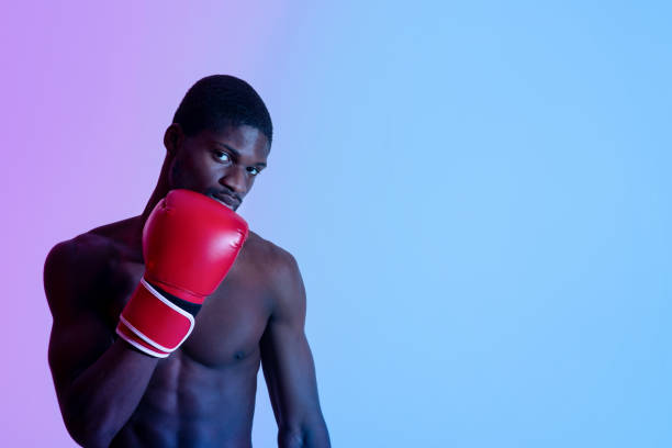 istock Determined young black boxer with bare torso wearing fighting gloves, looking at camera in neon light, copy space 1319048663