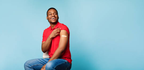 African American Guy Showing Arm After Vaccine Injection, Blue Background I'm Vaccinated. Joyful African American Guy Rolling Up Sleeve Showing Arm After Vaccine Injection Shot With Plaster On Blue Background. Health, Immunization And Vaccination. Panorama, Empty Space adhesive bandage stock pictures, royalty-free photos & images
