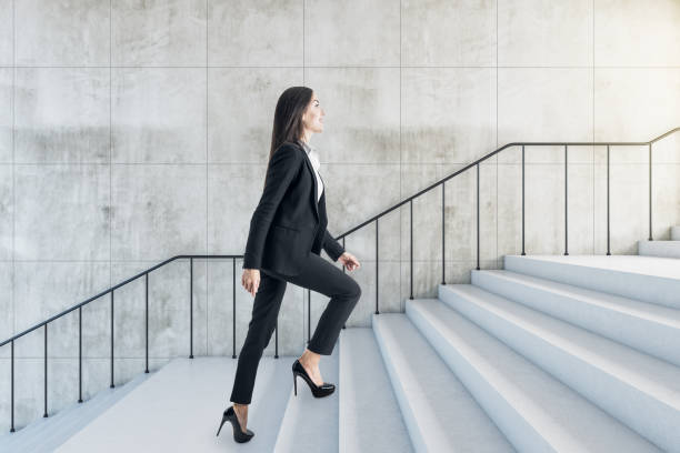 el concepto de éxito profesional con una mujer joven sube las escaleras a la luz en un edificio abstracto con elegante pared y escalera ligera. - escalón y escalera fotografías e imágenes de stock