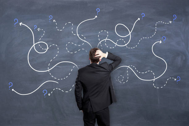 istock Right decision concept with man in black suit looking at chalkboard with painted dotted curved lines with question marks. 1319049419