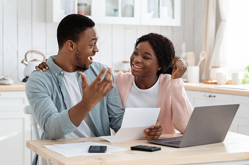 Portrait Of Happy Excited Black Married Couple Reading Insurance Documents In Kitchen, Joyful African American Family Celebrating Success, Got Taxes Refund Or Work Promotion Letter, Closeup