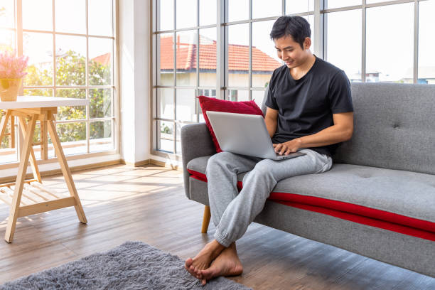 istock Happy young Asian man using laptop computer sitting o sofa in living room, work from home concept. 1319050670