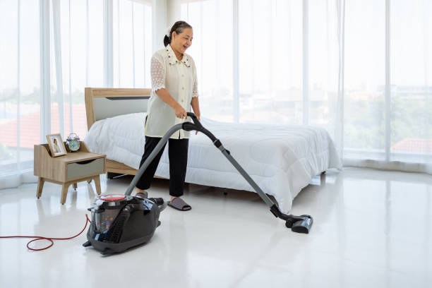 happy asian senior female woman cleaning bedroom floor with vacuum cleaner - senior getting groomed studio imagens e fotografias de stock