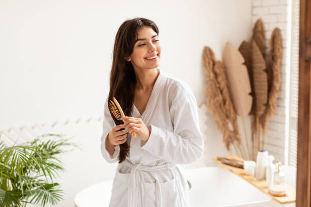 Brunette Woman Brushing Hair With Wooden Hairbrush In Modern Bathroom Haircare Concept. Brunette Woman Brushing Smooth Hair With Wooden Hairbrush Smiling Looking Aside Posing Wearing Dressing Gown In Modern Bathroom At Home. Hair Detangling And Beauty Routine hairbrush hair stock pictures, royalty-free photos & images