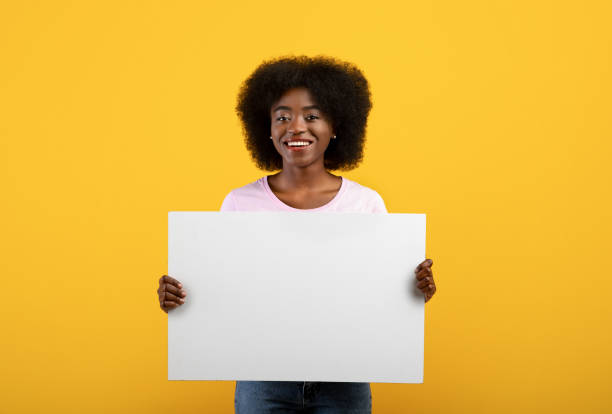 istock Advertisement concept. Excited black lady holding empty blank board isolated on yellow studio background 1319051722