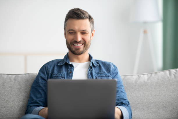 istock Closeup of positive bearded man using laptop at home 1319052183