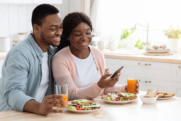 istock Millennial Black Man And Woman Having Breakfast And Using Smartphone In Kitchen 1319053036