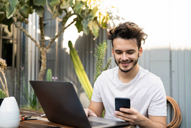 istock Portrait of smiling landscape gardener reading content on mobile phone while working on laptop in patio 1319054177