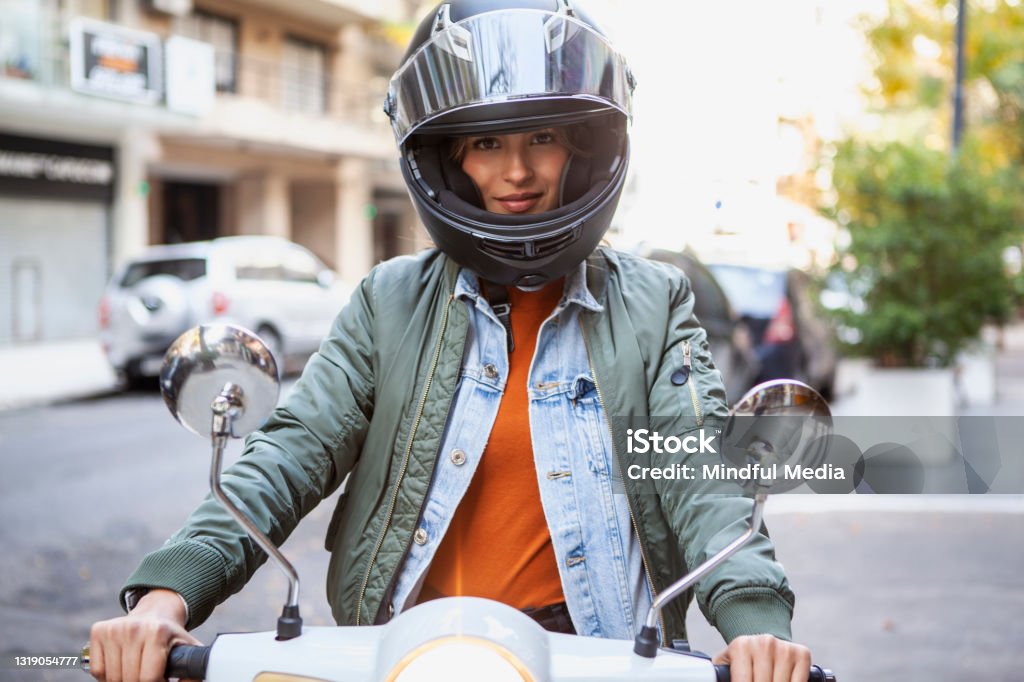 Portrait of smiling woman wearing crash helmet while sitting on motorcycle on the street during daytime Cheerful woman wearing crash helmet sitting on motorbike outdoors Motorcycle Stock Photo