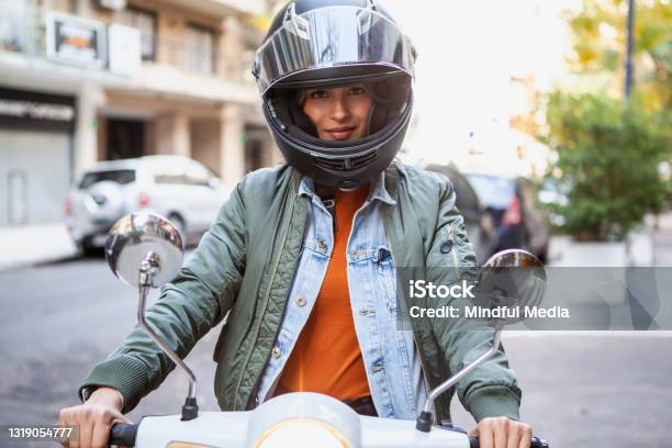 Portrait Of Smiling Woman Wearing Crash Helmet While Sitting On Motorcycle On The Street During Daytime Stock Photo - Download Image Now