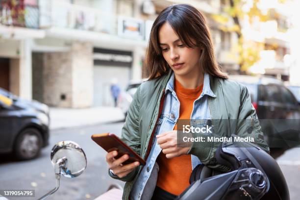 Portrait Of Young Delivery Woman Text Messaging While Standing Next To Motorcycle In The Street Stock Photo - Download Image Now