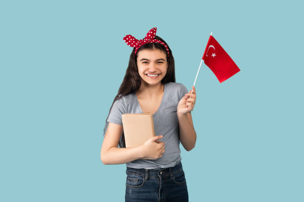 Happy Indian teen girl holding notebooks and showing flag of Turkey over blue studio background Happy Indian teen girl holding notebooks and showing flag of Turkey over blue studio background. Joyful teenage exchange student studying Turkish language abroad, immigrating to foreign country Study Abroad Countries stock pictures, royalty-free photos & images