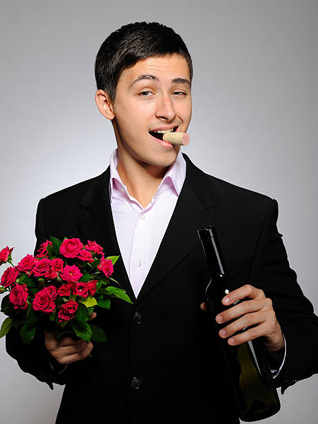 Handsome romantic young man holding rose flower and vine bottle stock photo