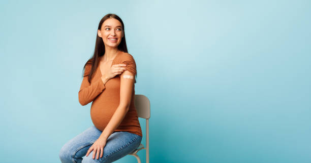 femme enceinte vaccinée affichant le bras après injection de vaccin, fond bleu - human pregnancy photos et images de collection
