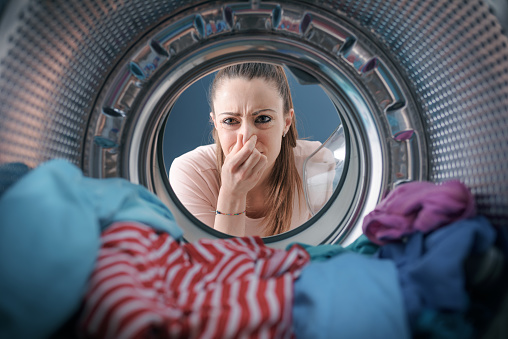 Woman staring at the laundry in the washing machine and holding her nose
