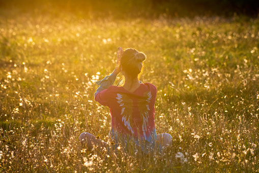 A woman is meditating during sunset hour in a grass field.