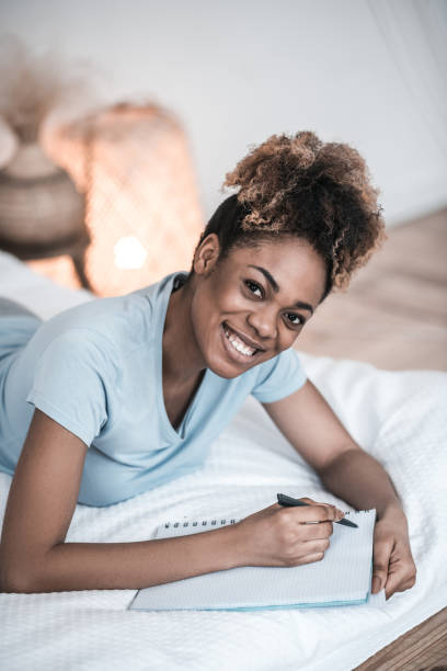 istock Darkskinned woman writing with pen while lying on bed 1319061107