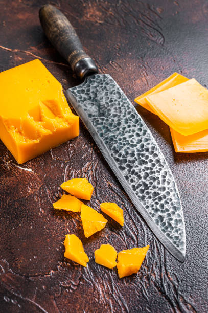 istock Cheddar Cheese sliced on a kitchen table with knife. dark background. Top view 1319061274