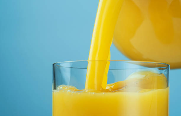 istock Orange juice pouring from jug into glass 1319068584
