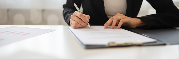 Wide view closeup image of a businesswoman signing a document or application form in a folder.