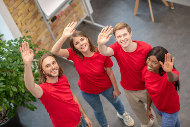 istock Team of young volunteers waving hand while standing indoors 1319072194