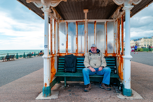 Brighton, UK - 17 May, 2021: a senior man sitting inside a shelter on the seafront of Brighton, UK. The man is sheltering from the storm and rain which is about to start.