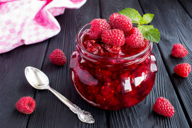 Raspberry jam in the glass jar on the  black wooden  background Raspberry jam in the glass jar on the  black wooden  background. Close-up. raspberry jam stock pictures, royalty-free photos & images