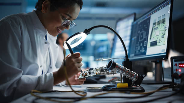 istock Modern Electronics Facility: Beautiful Black Female Scientist, Engineer Does Printed Curcuit Motherboard Soldering. Does Design, Development of Industrial PCB, Silicon Microchips, Semiconductors 1319077210