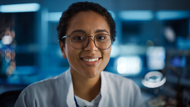 schöne schwarze latin frau trägt brille lächelnd charmant blick auf die kamera. junge intelligente wissenschaftlerin, die im labor arbeitet. technologische bokeh blau hintergrund. nahaufnahme schuss - charmingly stock-fotos und bilder