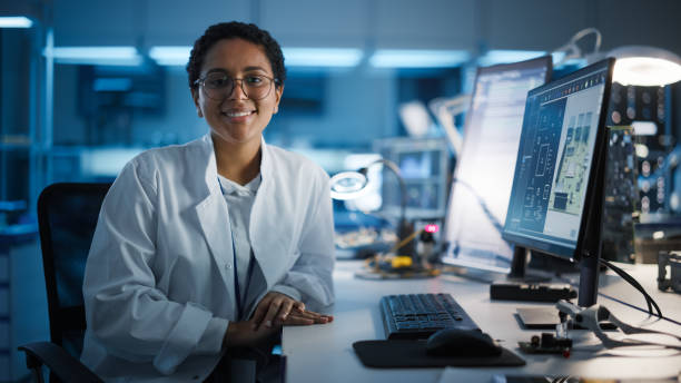 belles lunettes latines noires de femme s’usant souriant avec charme regardant l’appareil-photo. jeune scientifique femelle intelligente travaillant en laboratoire. laboratoire technologique à bokeh blue comme arrière-plan - charmingly photos et images de collection