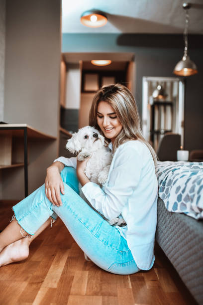 istock Cute Female Embracing Pet Dog While Sitting On Bedroom Floor 1319082524