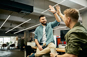 Happy creative business colleagues giving high-five to each other while working in the office.