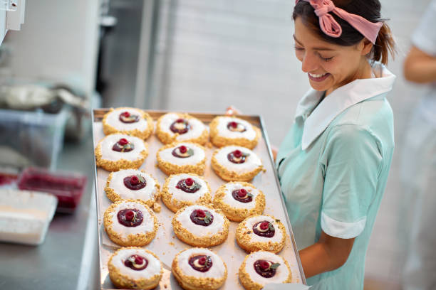 istock A beautiful retro looking young girl in a candy workshop holding and looking at a tray with delicious donuts ready for a pastry shop. Pastry, dessert, sweet, making 1319084029