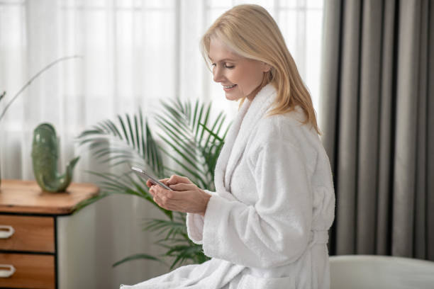 istock A woman in a white bath robe texting on a smartphone 1319084900