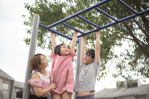 Asian Chinese mother and children playing on monkey bars public park.