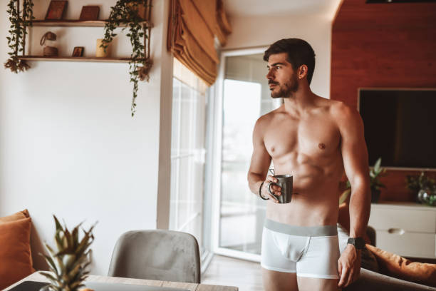 мужчина носить нижнее белье питьевой кофе в домашней гостиной - underwear men mens underpants male стоковые фото и изображения