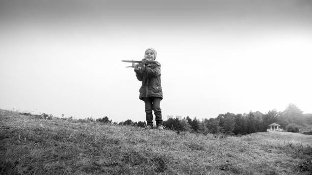 imagem em preto e branco de menino sorridente em pé no topo da colina e jogando aitplane de brinquedo - airplane black and white fun child - fotografias e filmes do acervo