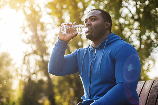 Man drinking water after exercise while resting on  bench.