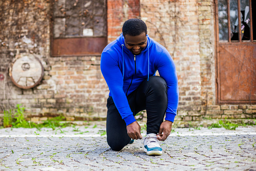 Young sporty man is tying shoelace outdoor.