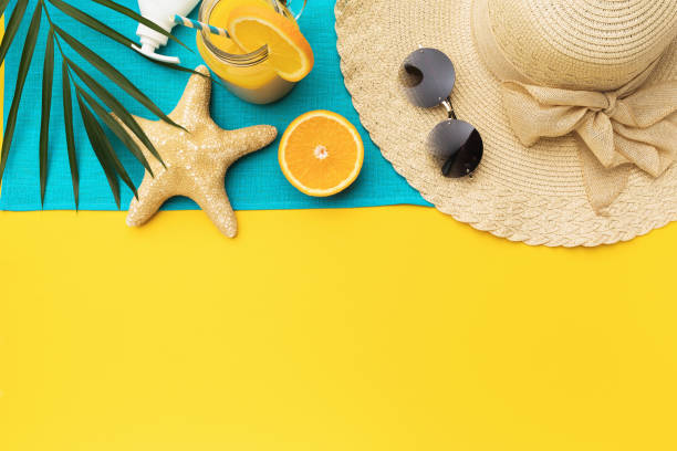 istock Beach holiday accessories, orange juice and palm leaf on a yellow background with a copy of space, summer background 1319089513